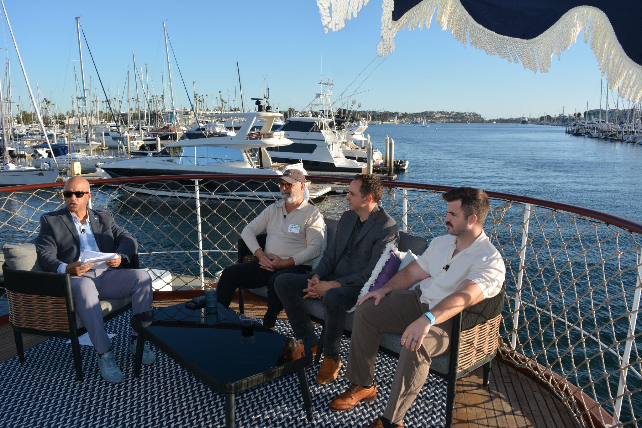 The fireside chat panel seated on the yacht deck with the marina behind them.